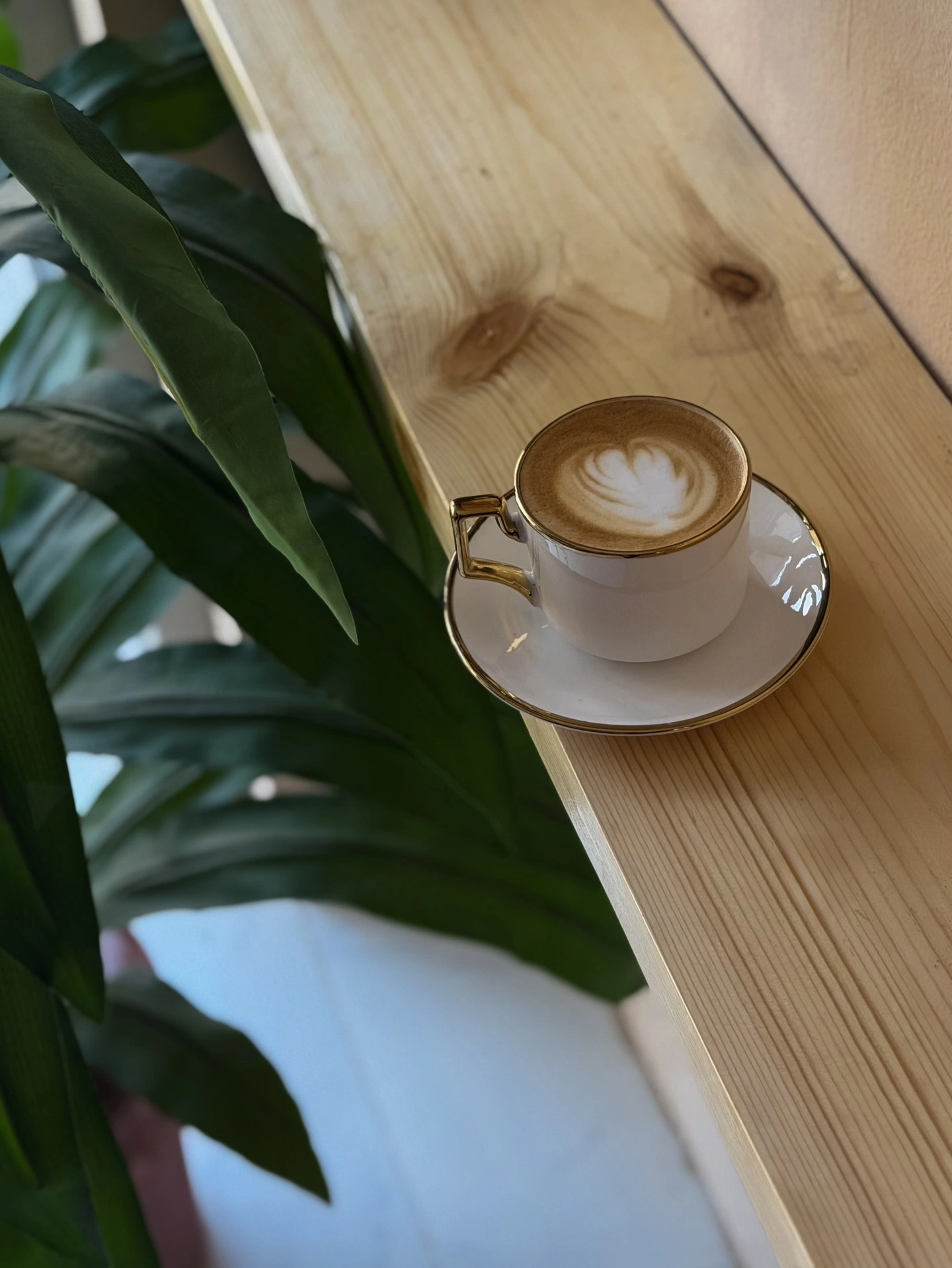 Latte art in a gold-rimmed cup on a wooden table at Aroma Cafe