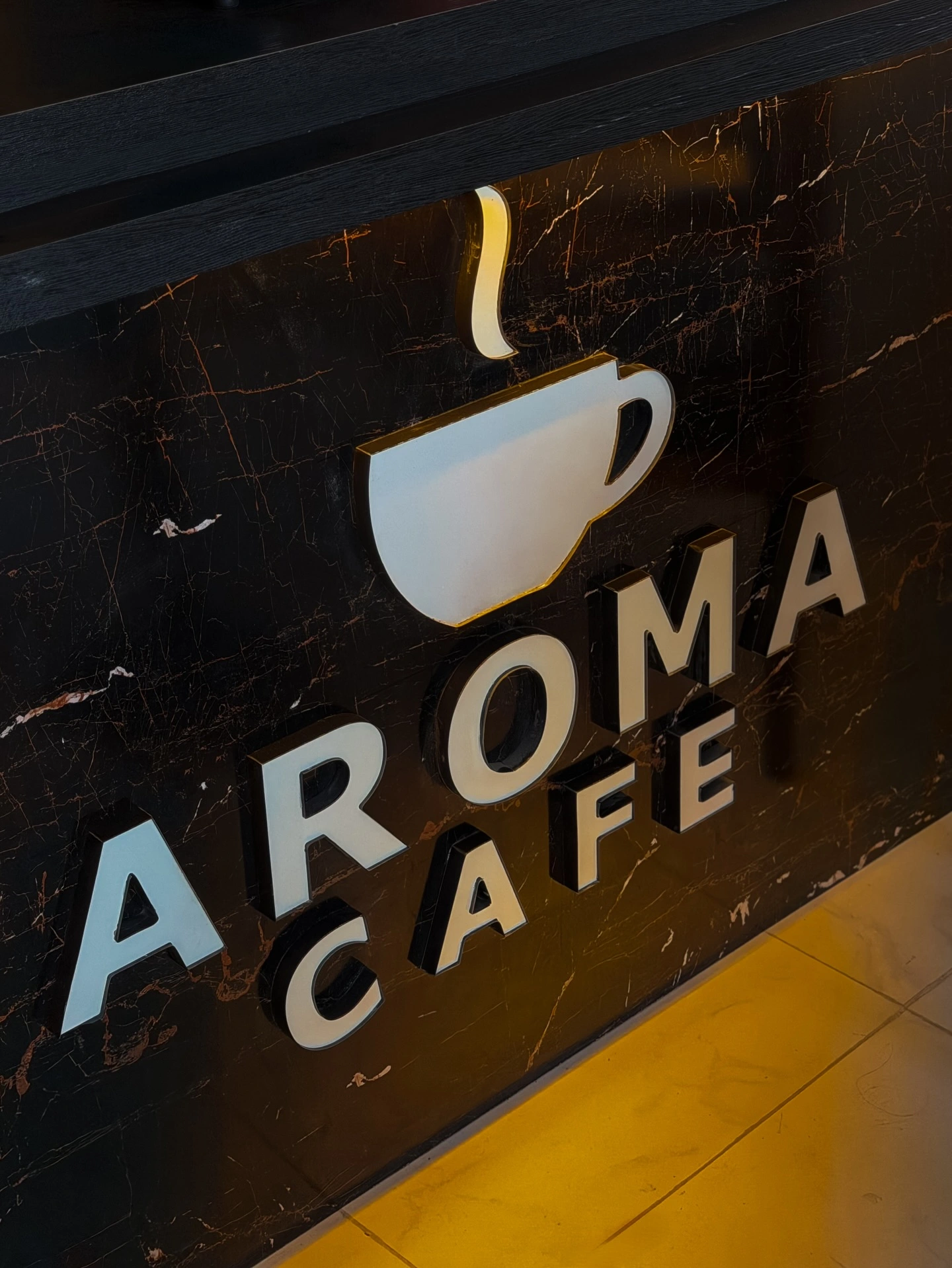 The illuminated Aroma Cafe logo sign on dark marble