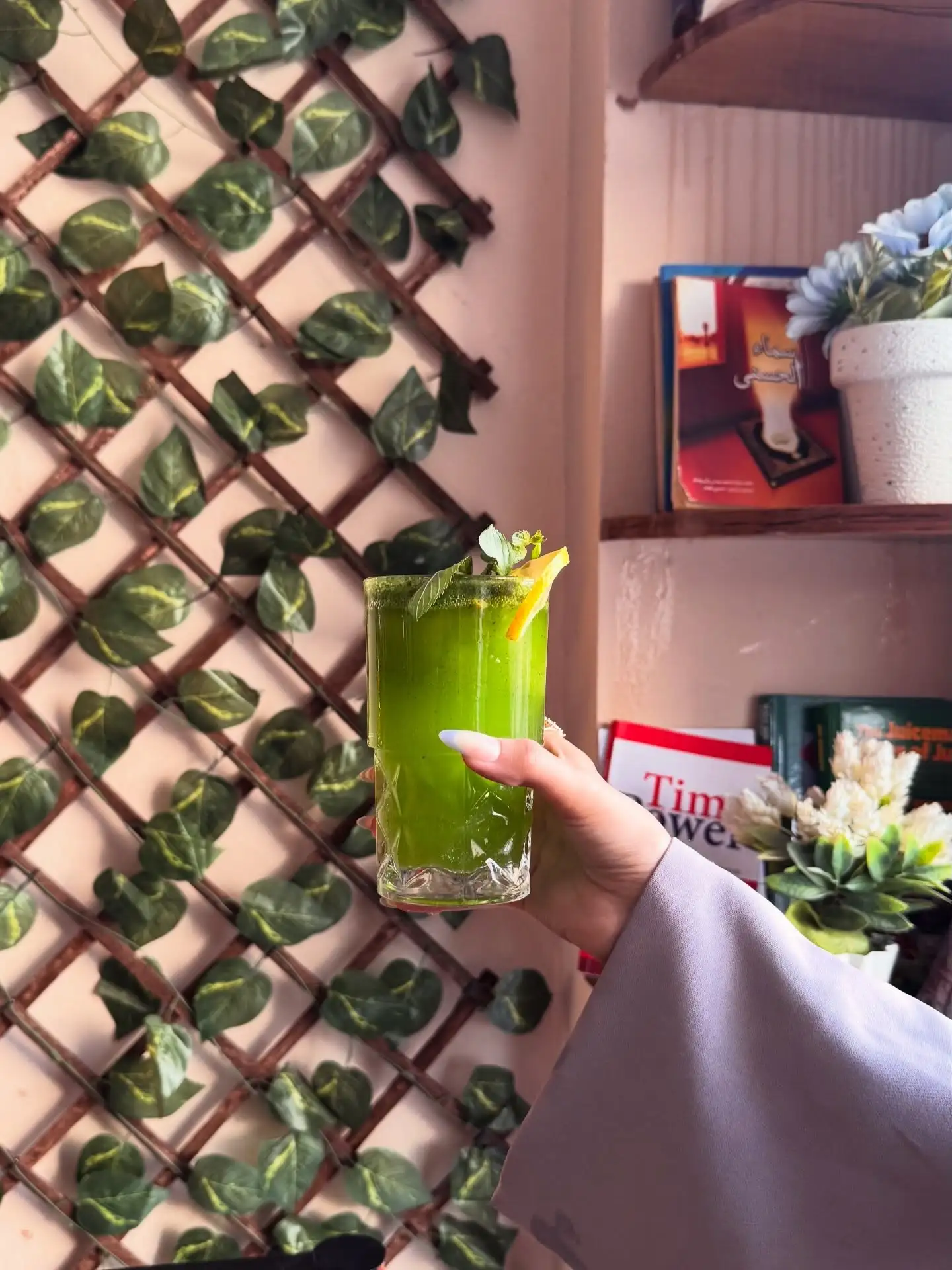 Fresh green mint drink held in front of a leafy wall