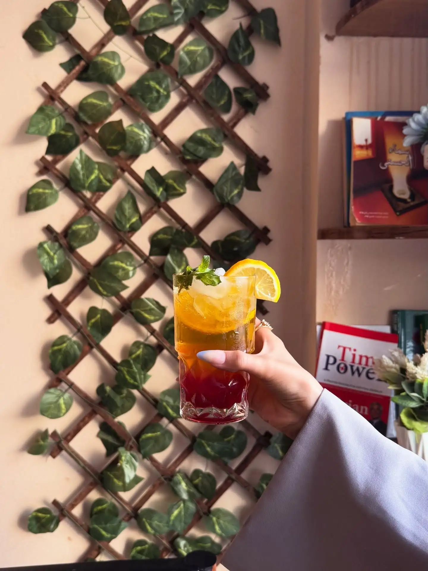 Layered citrus mojito with mint held beside a leafy wall