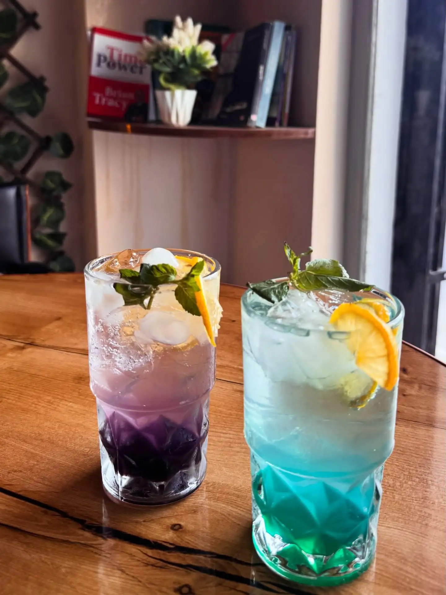 Two layered iced drinks with mint and orange on a wooden table